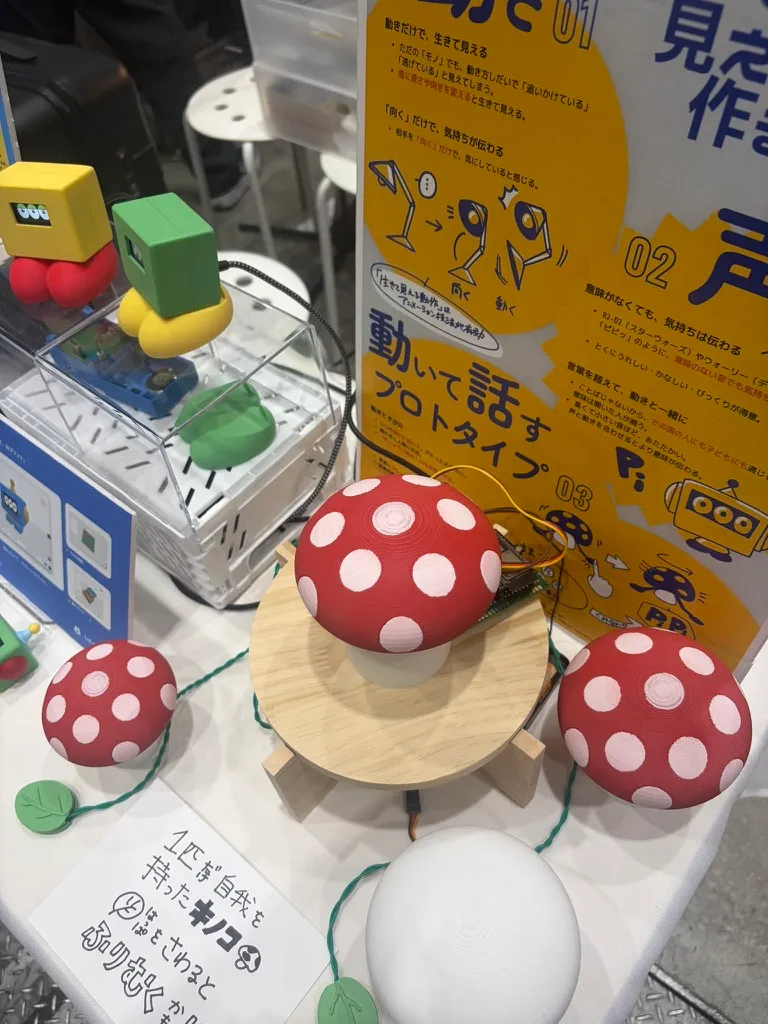 The red mushroom robot next to yellow and green Sankome robots, with a poster about movement and voice behind them