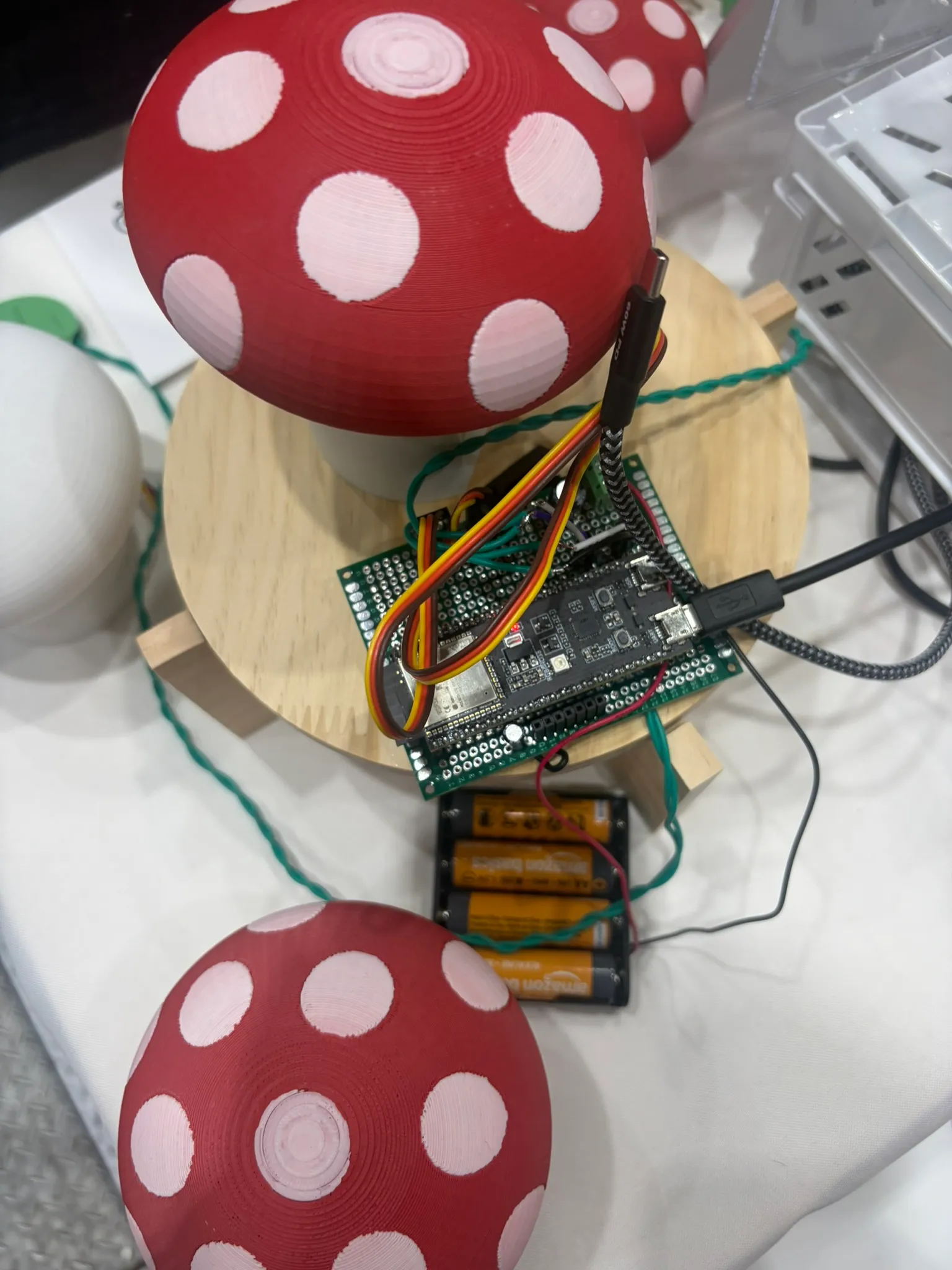 A perfboard next to the mushroom robot, with an ESP32-S3, wires, capacitors, and a battery holder